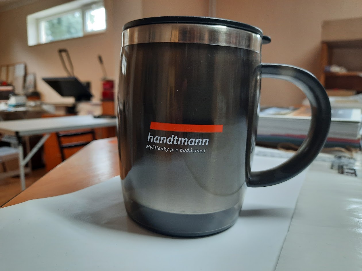 Kovový termohrnček s čiernym uchom a logom Handtmann